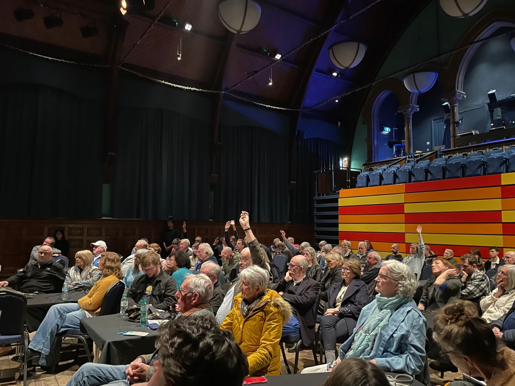A packed audience at the Haverhill Arts Center with hands raised for questions
